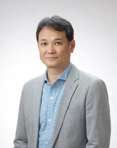 A portrait of Prof. Hiroaki Ogata in a grey suit and light blue shirt.